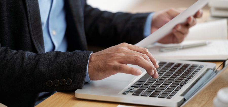 Hands of businessman checking document and typing on keyboard