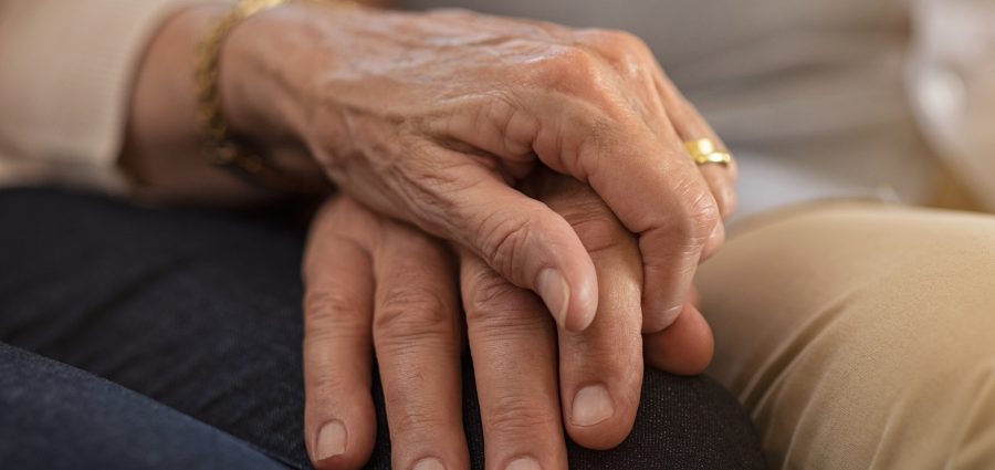 Closeup of elderly couple holding hands while sitting on couch. Husband and wife holding hands and comforting each other. Love and care concept.